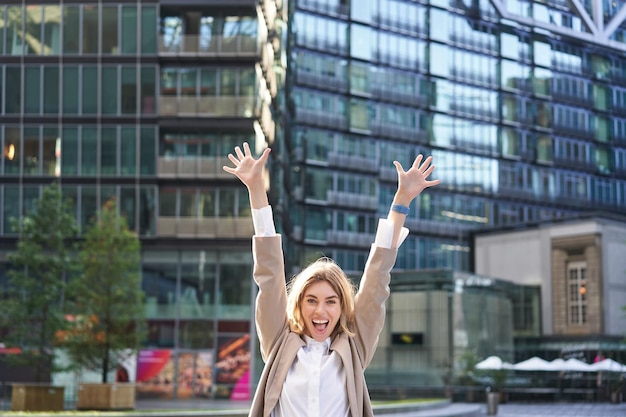 Corporate woman celebrating her victory outside on street happy businesswoman raising hands up and t