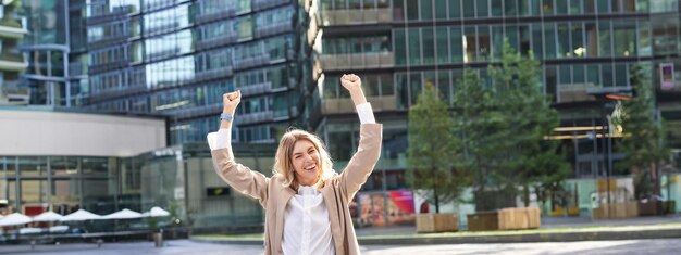 Corporate woman celebrating her victory outside on street happy businesswoman raising hands up and