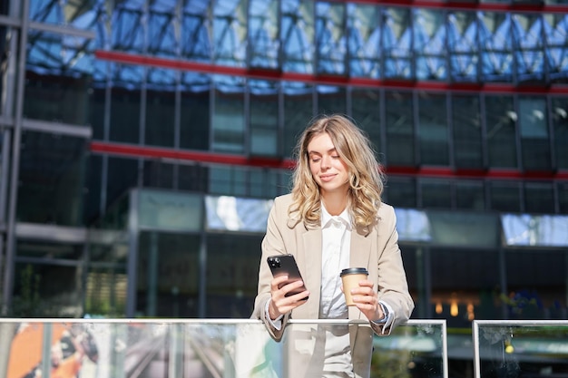 Free photo corporate woman drinking her coffee and looking at mobile phone businesswoman relaxing on her lunch