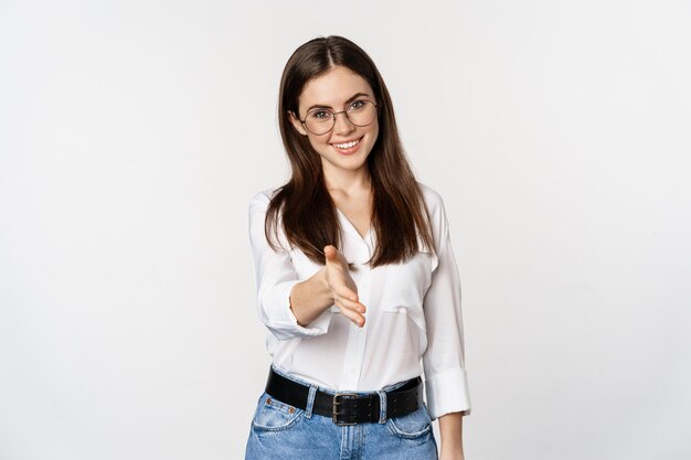 Corporate woman in office extending hand and smiling handshake greeting business partner standing in...