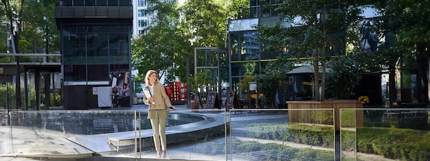 Корпоративная женщина в костюме уверенно стоит в бежевом костюме с рабочими документами на открытом воздухе