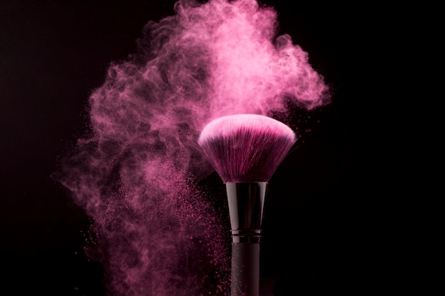 Cosmetic brush in cloud of pink powder on dark background