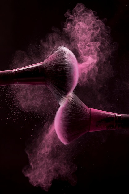 Cosmetic brushes in pink mist of powder on dark background