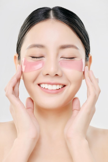 Maschera per gli occhi cosmetica close up beauty face donna asiatica con pelle fresca e pulita utilizzando eye pad trattamento per la cura degli occhi isolato su bianco concetto di bellezza e cura della pelle