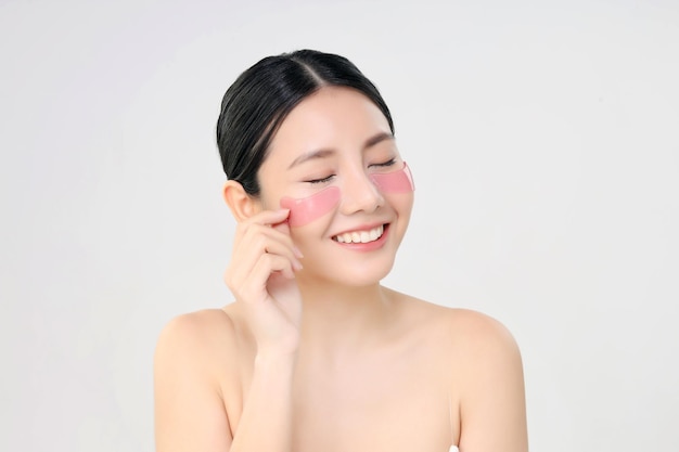 化粧品のアイマスクは、白い美容とスキンケアのコンセプトで分離されたアイパッドアイケアトリートメントを使用して新鮮なきれいな肌を持つ美容顔アジアの女性をクローズアップ