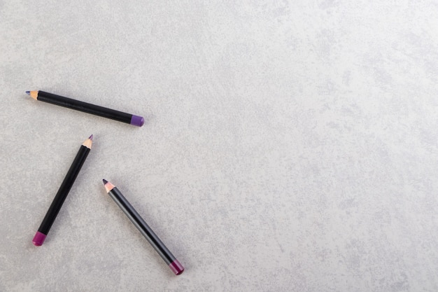 Cosmetic pencils of make up placed on a stone table .