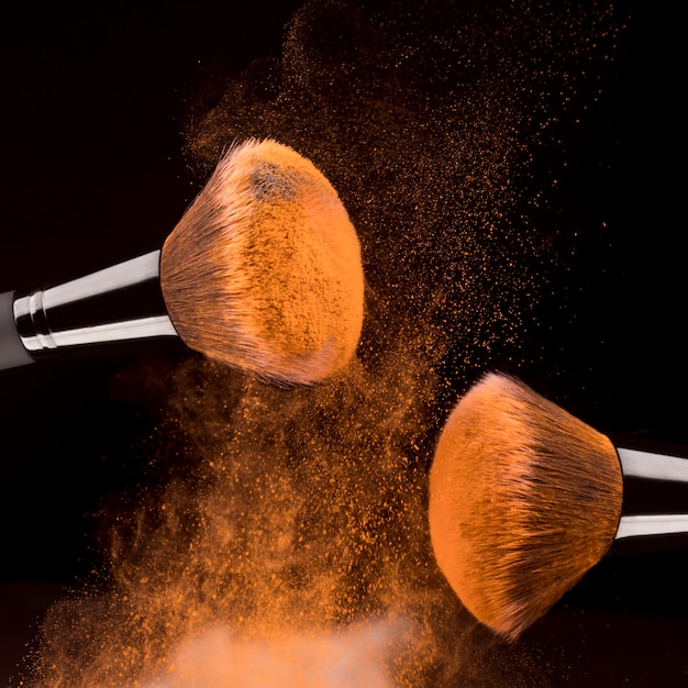 Cosmetic tools and orange powder on black background