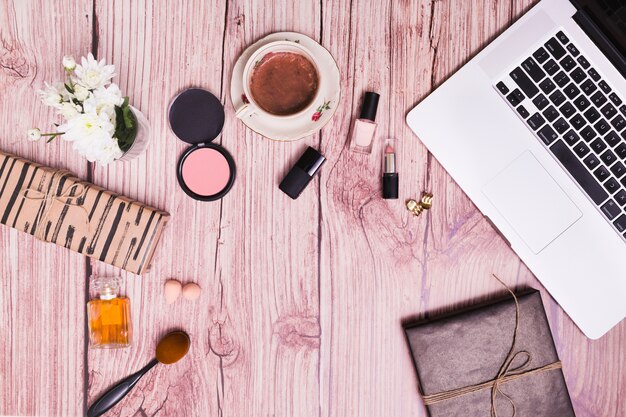 Cosmetics products; vase; diary and laptop on pink wooden textured background