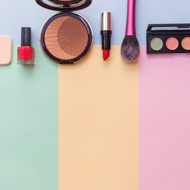 Cosmetics sponge; nail varnish bottle; lipstick; blusher and eye shadow palette on mixed colored background