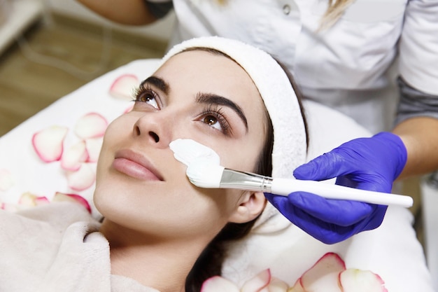 Cosmetologist applies white mask on woman's face