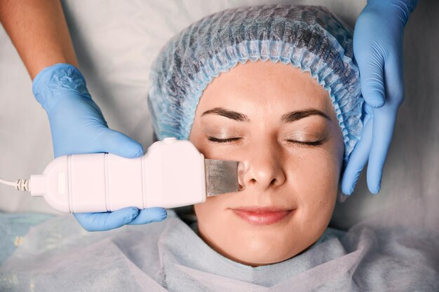 超音波スクラバーで女性の額を掃除する美容師