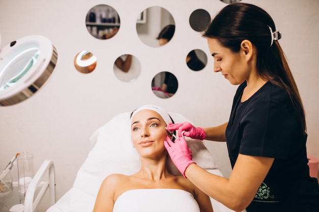 Косметолог делает уколы на лице женщины в салоне красоты