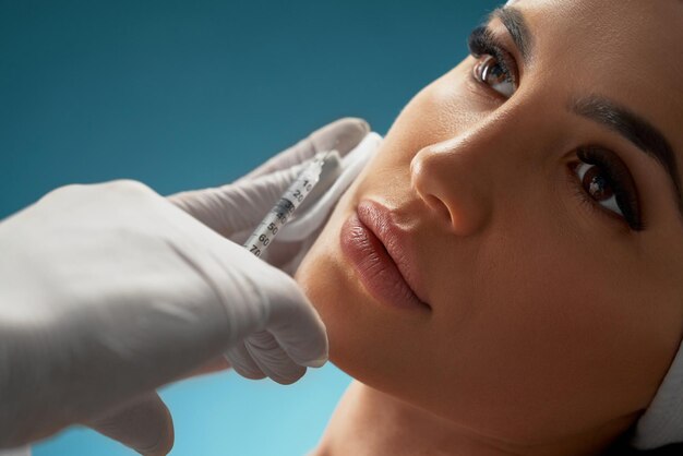 Cosmetologist using syringe to correct female face