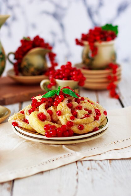 Cottage cheese cookie rolls with red currants on ceramic plate with vintage ceramic tea or coffee set, tea time, breakfast, summer sweets