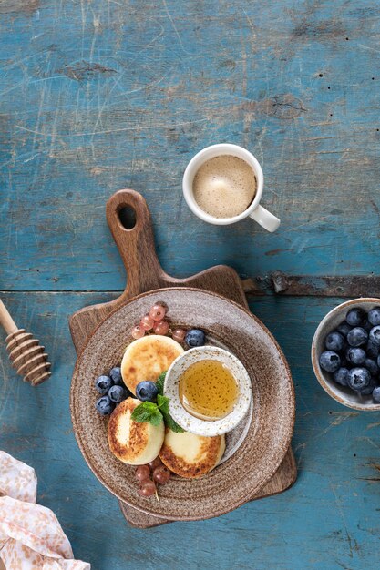 Cottage cheese pancakes cheesecakes ricotta fritters with fresh blueberries currants and peaches on a plate Healthy and delicious breakfast for the holiday Blue wooden background