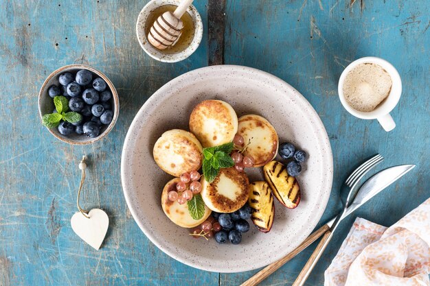 Cottage cheese pancakes cheesecakes ricotta fritters with fresh blueberries currants and peaches on a plate Healthy and delicious breakfast for the holiday Blue wooden background