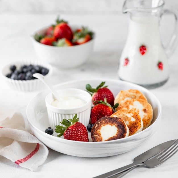코티지 치즈 팬케이크 치즈 케이크 리코타 프리터, 흰색 세라믹 접시에 담긴 신선한 딸기와 블루베리를 곁들인 휴가를 위한 건강하고 맛있는 아침 식사
