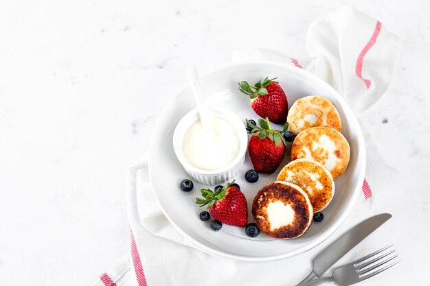 Cottage cheese pancakes cheesecakes ricotta fritters with fresh strawberries and blueberries from a white ceramic plate Healthy and delicious breakfast for the holiday