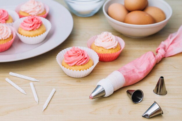 ノズル付きコットンアイシングバッグ。カップケーキ卵と木製の机の上のろうそく