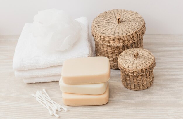 Cotton swab; soaps; towel; loofah and wicker basket on wooden tabletop