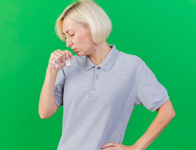 Coughing young blonde ill slavic woman holds tissue isolated on green