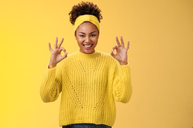 Count it done. Assured confident african-american woman in sweater headband show okay ok no worries gesture smiling self-assured plan goes fine, pleased good results, cheering yellow background.