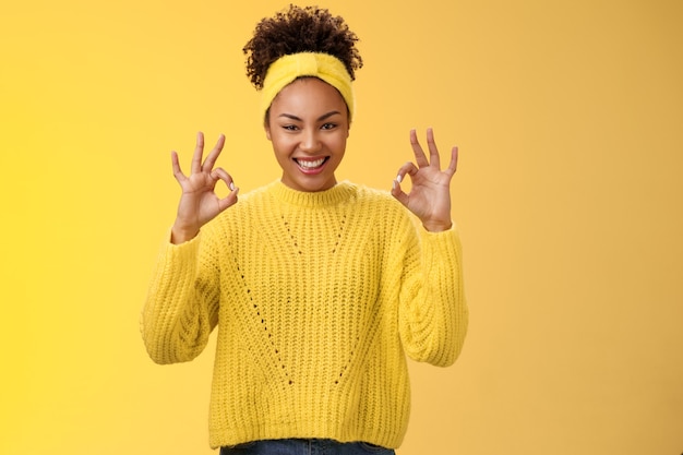 完了したと数えます。セーターのヘッドバンドで自信を持って自信を持ってアフリカ系アメリカ人の女性を見せて大丈夫OK心配しないジェスチャー笑顔自信のある計画はうまくいき、良い結果を喜ばせ、黄色の背景を応援します。