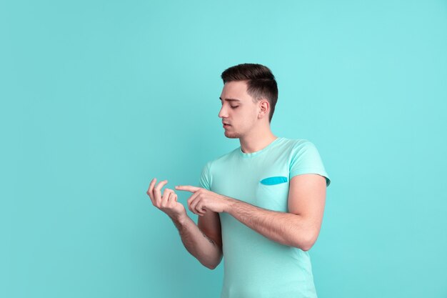 Counting on fingers. Caucasian young man's portrait isolated on blue studio wall