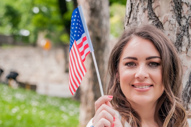 country, patriotism, independence day and people concept - happy smiling young woman in white dress with national american flag