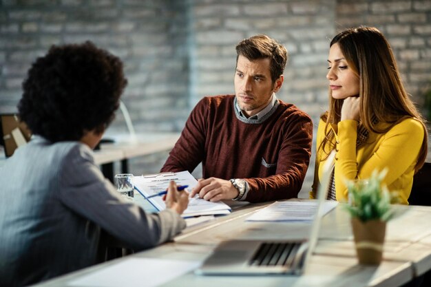 Couple analyzing mortgage agreement with their real estate agent during the meeting in the office Focus is on man