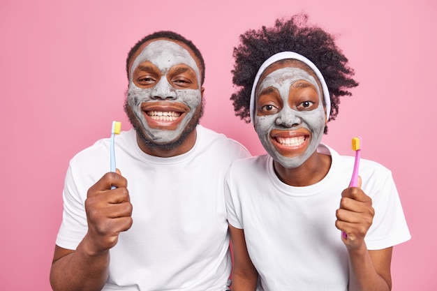пара наносит глиняные маски на лицо, чтобы уменьшить морщинки и удалить поры улыбка широко показать белые идеальные зубы после процедуры отбеливания держать зубные щетки заботиться о коже