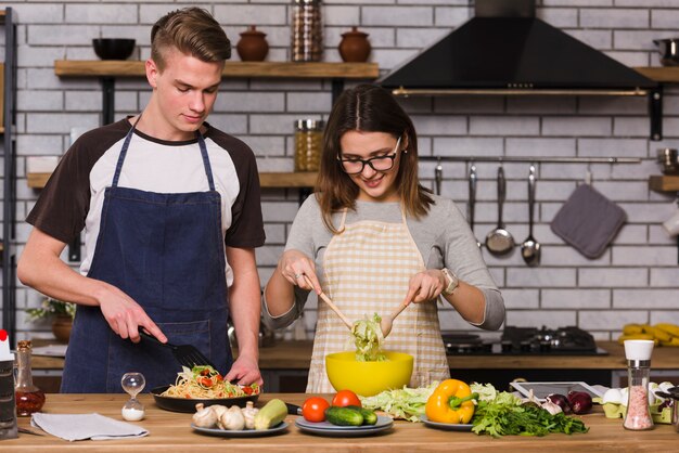 Couple in aprons cooking food in kitchen