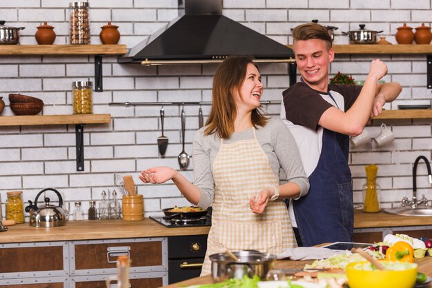 Couple in aprons having fun and dancing in kitchen