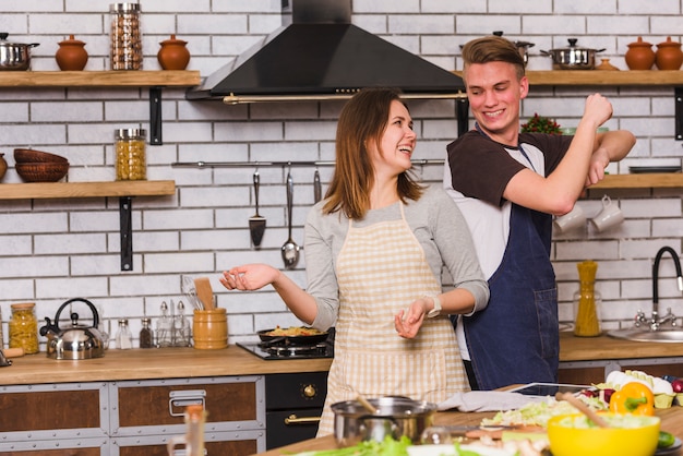 Couple in aprons having fun and dancing in kitchen