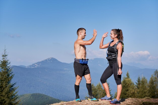 Пара спортивных улыбающихся друзей, стоящих на вершине горного холма