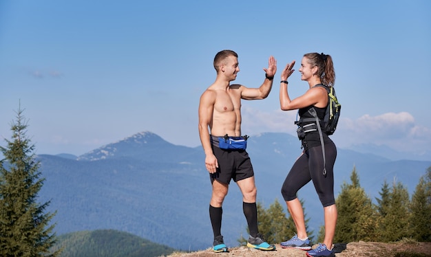 Couple of athletic smiling friends standing on top of mountain hill