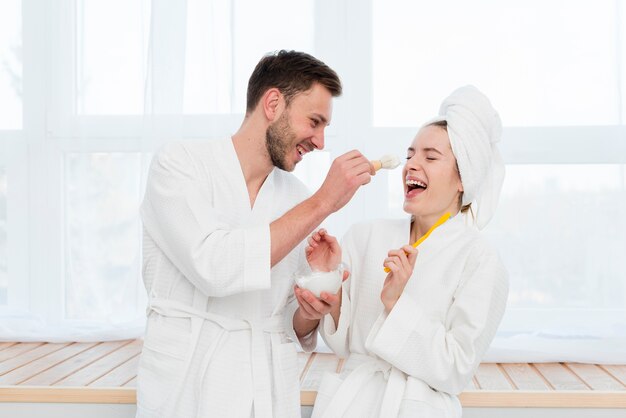 Couple in bathrobes fooling around with shaving foam