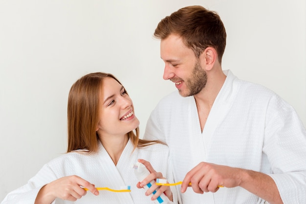 Couple in bathrobes holding toothbrushes and looking at each other