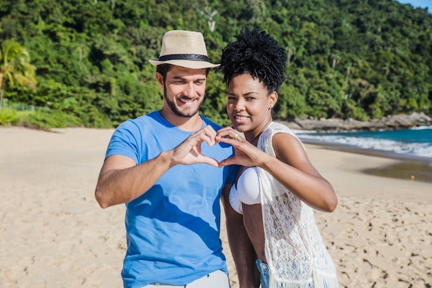 Couple at the beach forming heart with hands