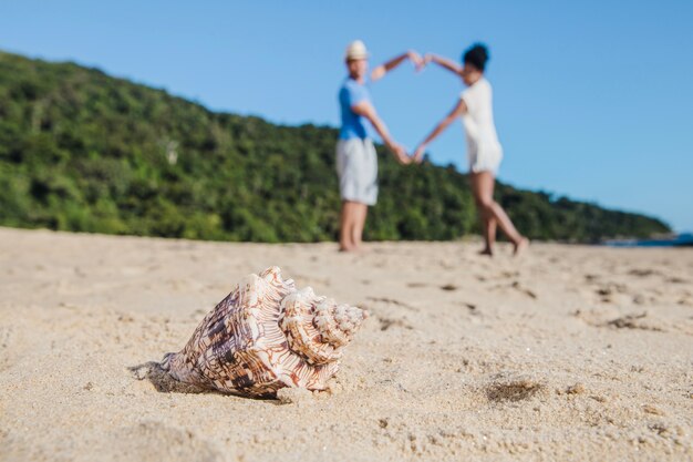 Couple at the beach forming heart with seashell in foreground