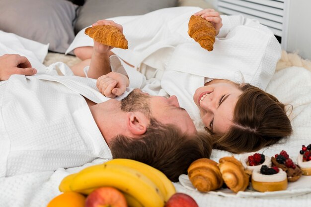 Couple in bed holding croissants