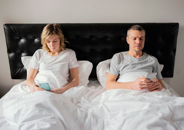 Пара в постели с помощью мобильных телефонов