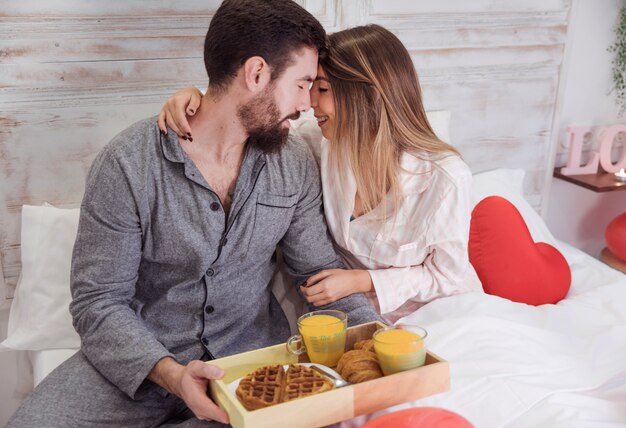 Couple on bed with breakfast on wooden tray