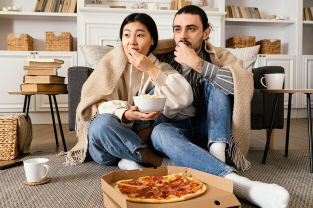 ピザとポップコーンを食べる毛布のカップル
