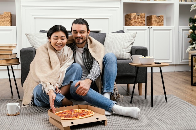 Couple in blanket watching tv and eating pizza