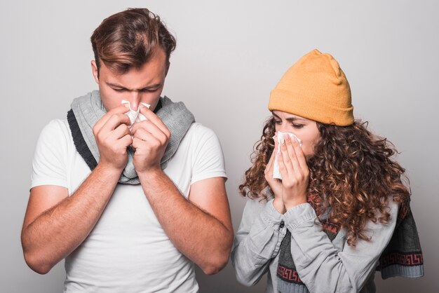 Couple blowing their nose with tissue paper on gray background