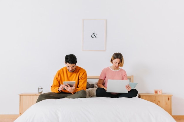 Couple browsing laptop and tablet on bed