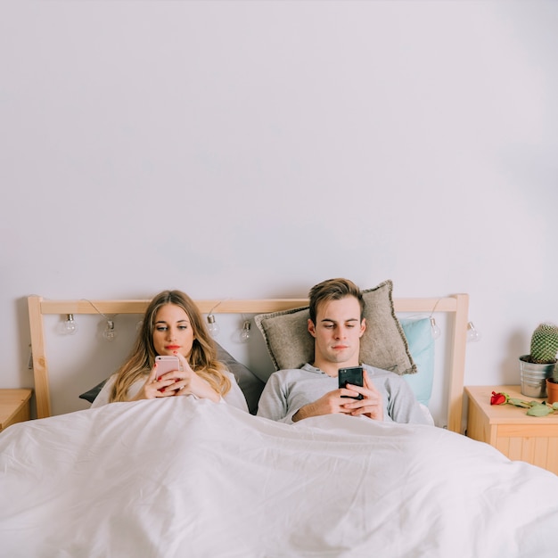 Пара просмотра смартфонов в постели