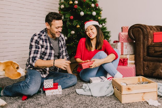 Couple celebrating christmas with dog in front of christmas tree