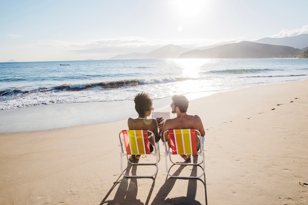 Couple chilling on deck chairs with at the beach